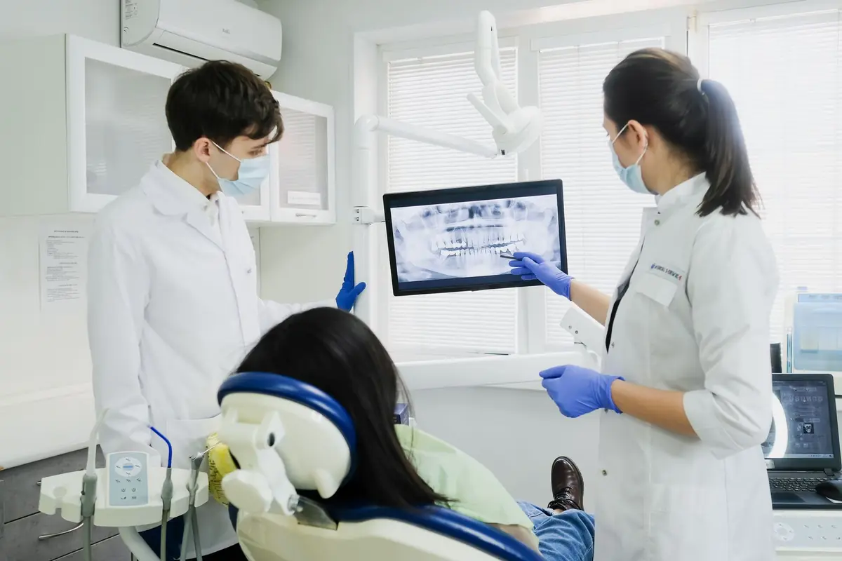 Two dental professionals look at an X-ray on a screen with a patient in the chair