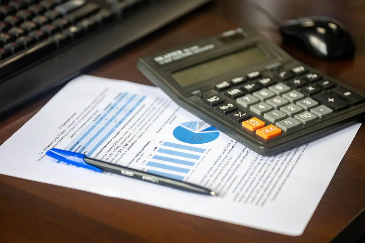 A calculator and pen resting on a printed financial report with charts