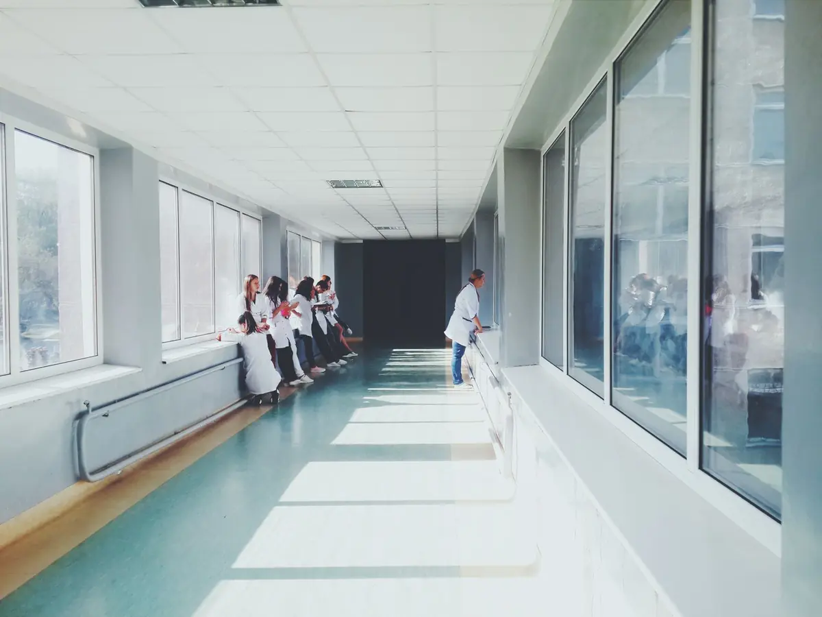 A long, brightly lit hospital corridor with medical staff in white coats in the distance