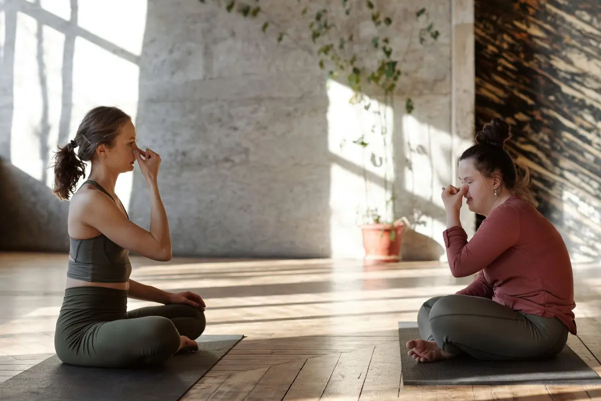Two women sitting cross-legged on mats practising a breathing exercise