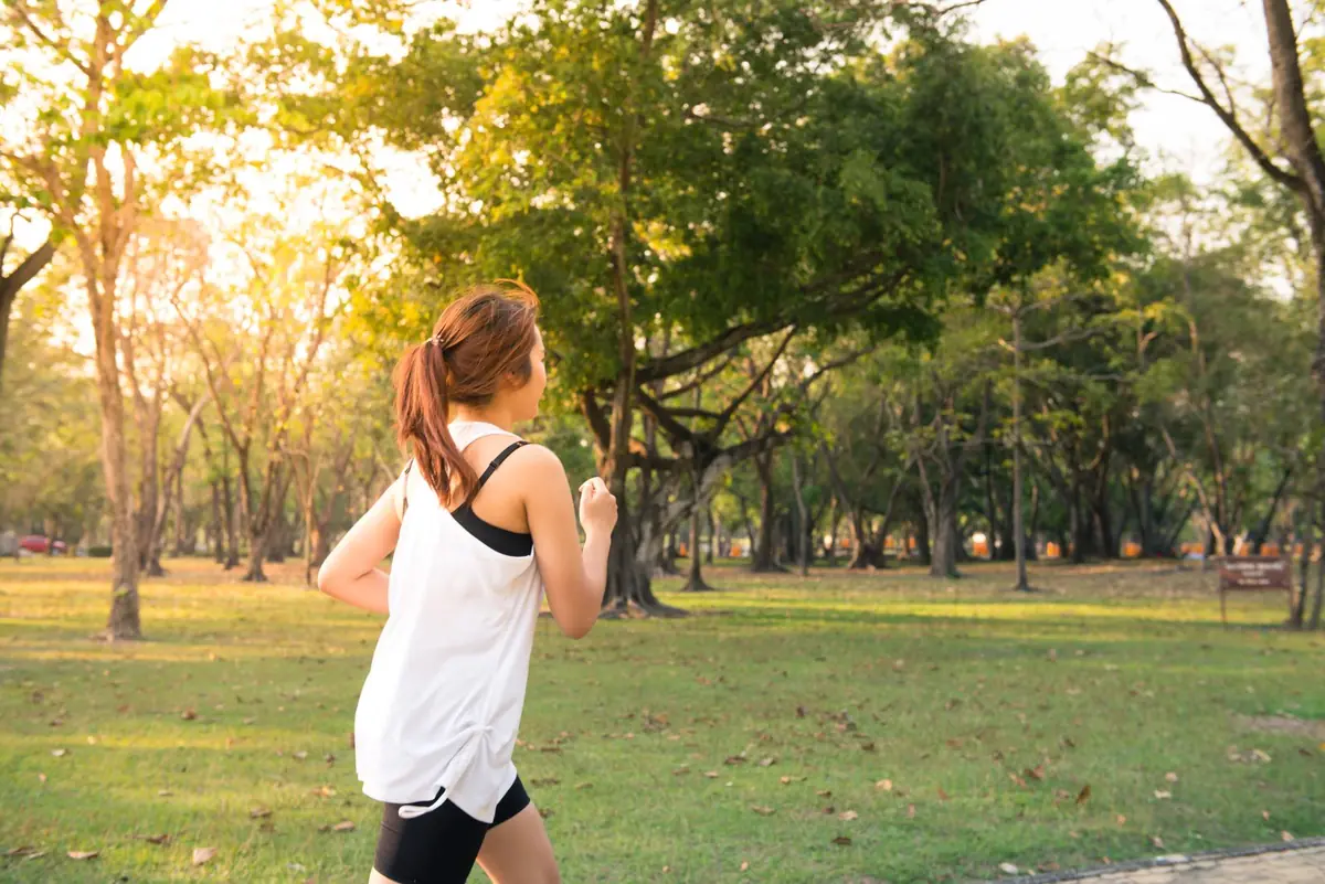A woman jogging through a park in warm morning light